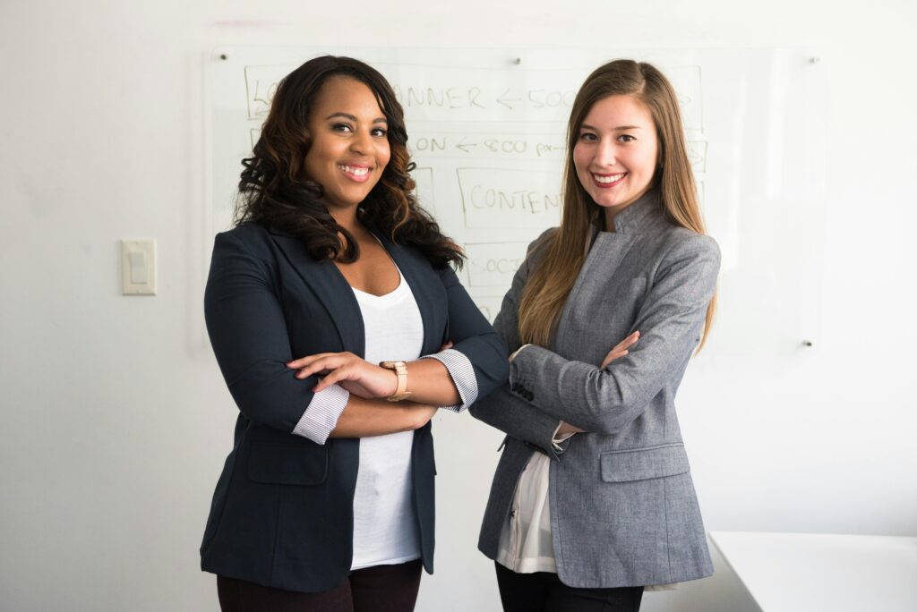 Two diverse businesswomen smiling confidently in a modern office environment.