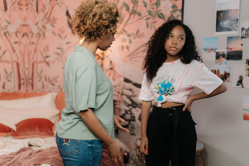 A mother and teen daughter in a tense conversation in a modern bedroom setting.